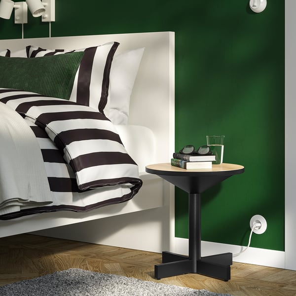 Small, modern GRIMSARBO bedside table against green wall next to white bed with striped black & white blanket.