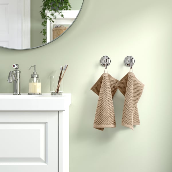 Beige GULVIAL towels hang on chrome hooks by bathroom sink with mirror.