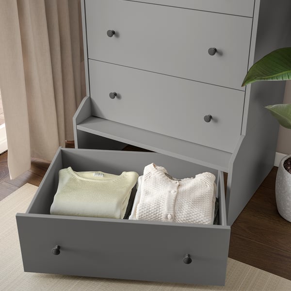 Grey chest of drawers with four drawers, three closed and one open displaying neatly folded clothes.