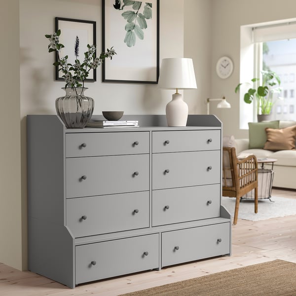Large grey HAUGA chest of drawers with 8 drawers in living room. Decorated with a vase and lamp. Wide drawers, simple design.