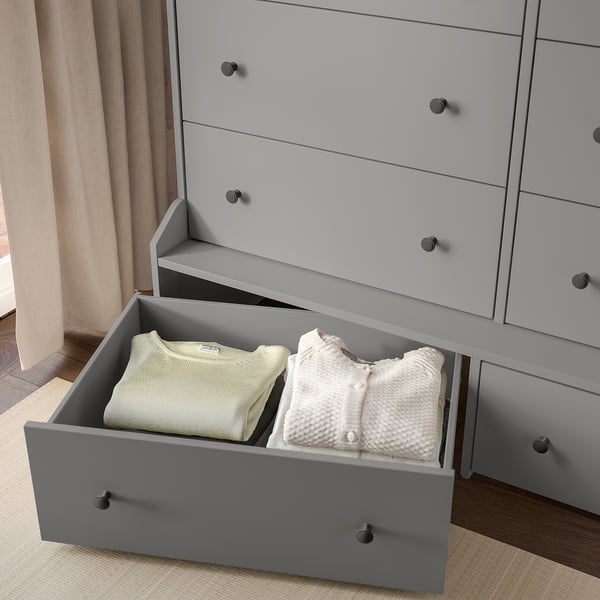 Open grey dresser with two folded sweaters in bottom drawer.