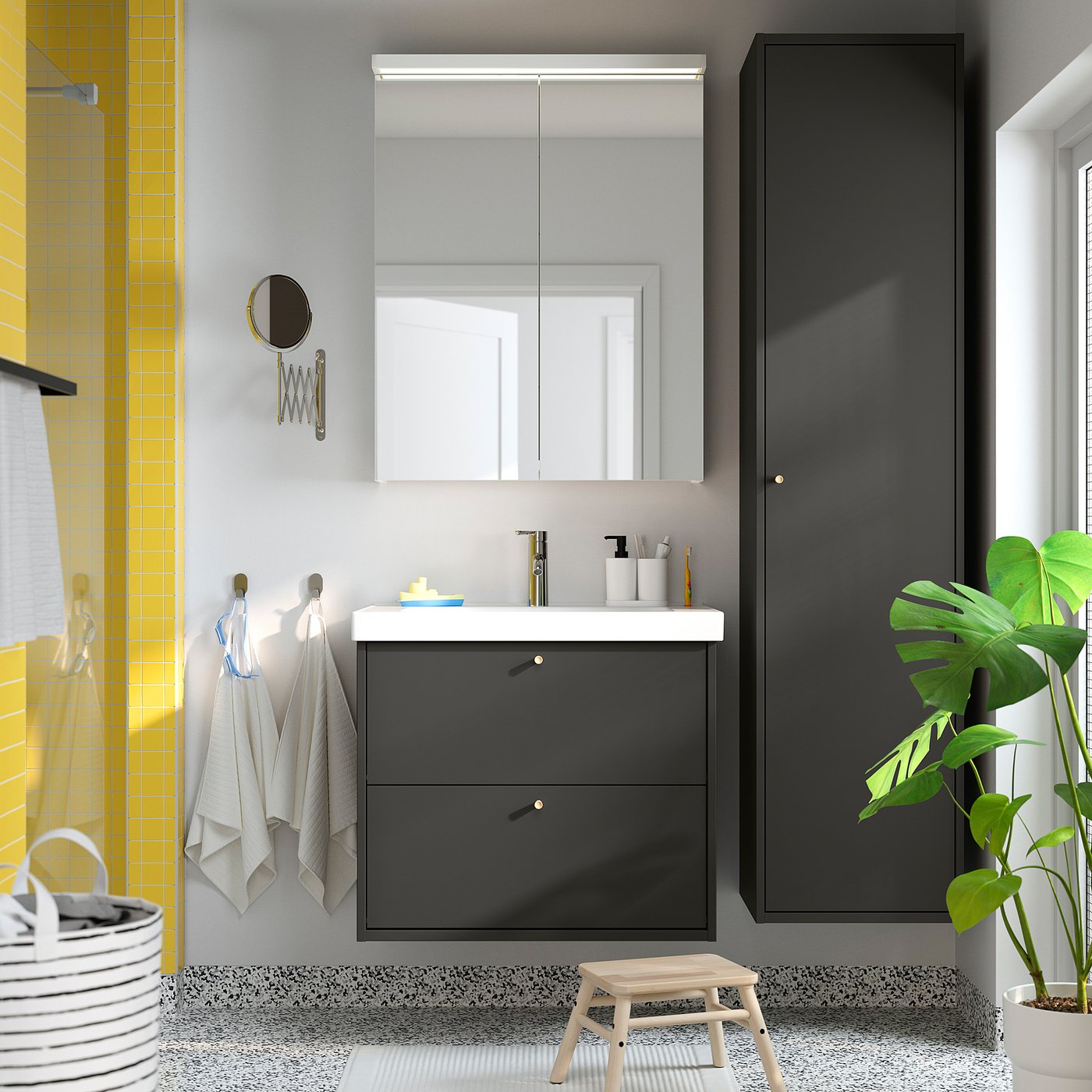 Modern grey bathroom with mirror cabinet, small sink, towels, plant, and step stool, emphasising compact storage.