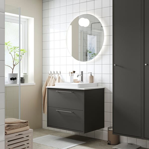 Modern bathroom with dark grey HAVBÄCK vanity, round mirror, white sink, and minimalist decor.