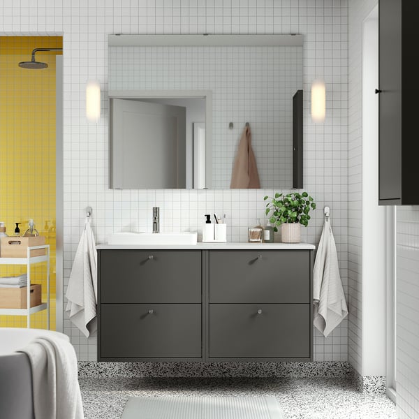 Modern bathroom with dark grey storage cabinet, multiple drawers, ceramic sink, and wall-mounted design under a large mirror with lights.