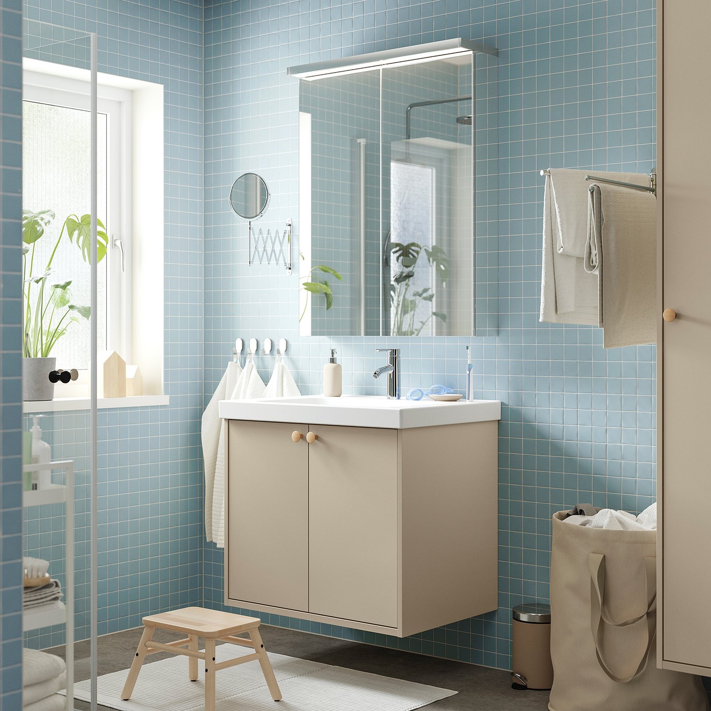 Bathroom with blue-tiled walls, beige HAVBÄCK vanity and white sink. Includes mirror, towels, plant, and wooden stool. Clean and minimalist design.