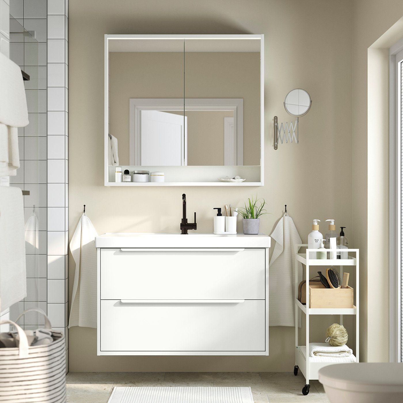 Modern bathroom with HAVBÄCK vanity, black tap, large mirror, and white cart with toiletries and plant.