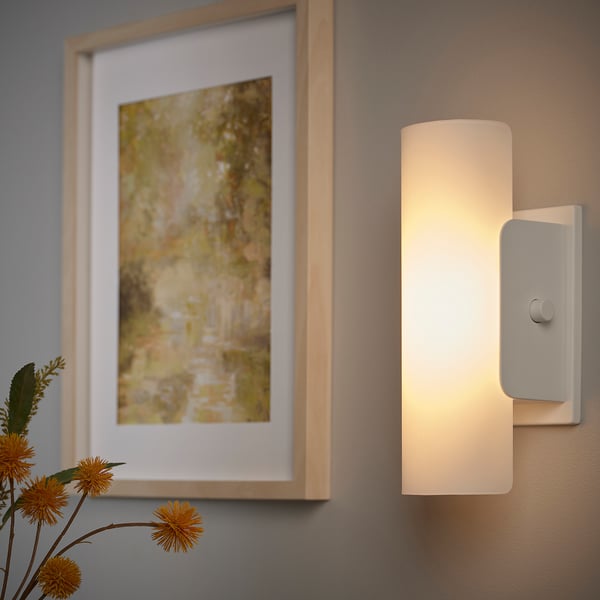 A modern wall lamp with a frosted glass shade emits soft, dimmable light next to a framed picture.
