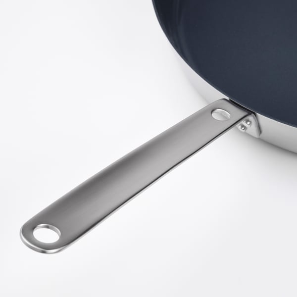 Silver frying pan handle attached to pan with rivets, showcasing sturdy, durable design.