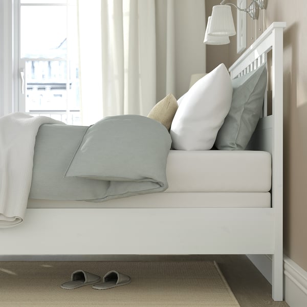 Bed with white headboard, grey pillows, slippers, and window.