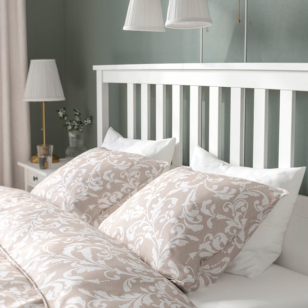 Bedroom scene with a HEMNES bed, featuring a high headboard and ornate pillows. White bedside lamp visible on left.