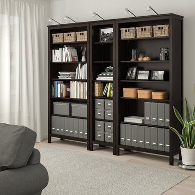 HEMNES black bookcases with shelves & storage boxes. Grey chair & plant nearby.