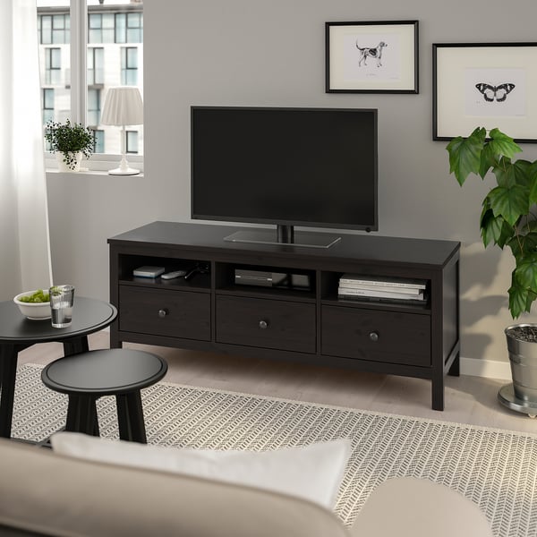 Modern living room with large HEMNES black-brown wood tv bench, flat screen tv, small round tables, plants, and artwork on grey wall.
