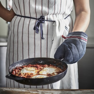 Person holding a skillet with cooked food wearing striped apron and oven mitt.