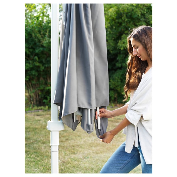 Person adjusts grey HÖGÖN parasol on lawn for shade.
