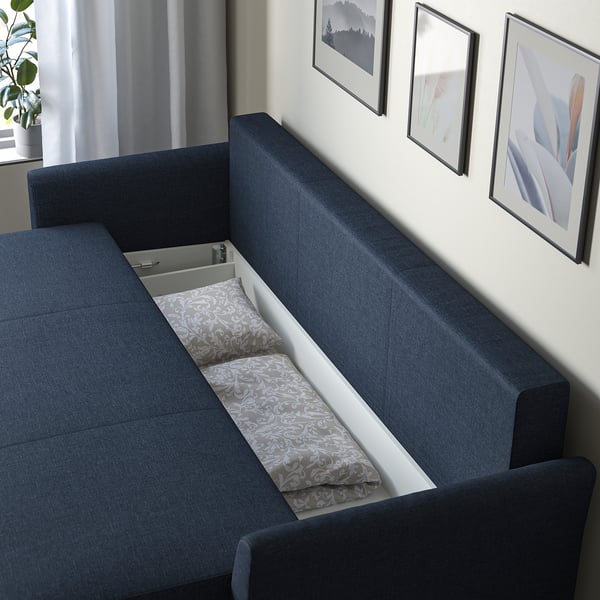 Blue sofa with a storage compartment open, displaying folded pillows inside. The compartment is beneath the seat, easily accessible.