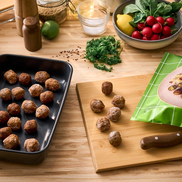 Wooden table with HUVUDROLL falafel, herbs, radishes, lemons, and kitchen tools.
