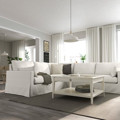 Modern living room with HYLTARP white sofa, cushions, grey rug. Coffee table centred, hanging lamps. Large window with curtains.