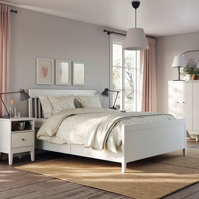 Modern bedroom with white IDANÄS bed, soft blankets, lamps, and botanical prints.