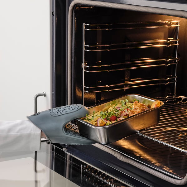 Stainless steel container with herbs & roasted chicken on oven, blue mitt for safe handling.