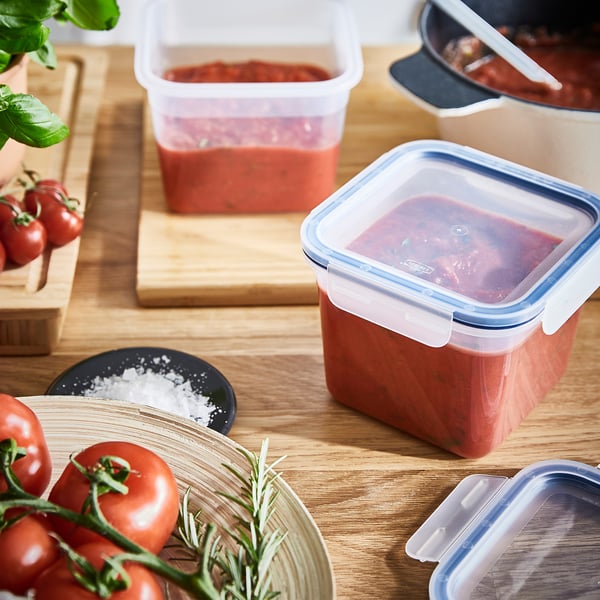 Plastic food containers in red, storing tomato sauce, on wooden table. Suitable for leftovers and stacks for space-saving.
