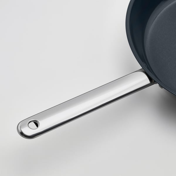 A sleek, modern frying pan with a shiny, silver stainless-steel handle, attached to a black pan resting on a white surface.