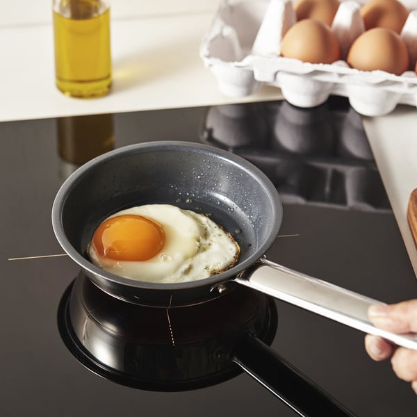 Black frying pan with non-stick coating on stove cooking egg.