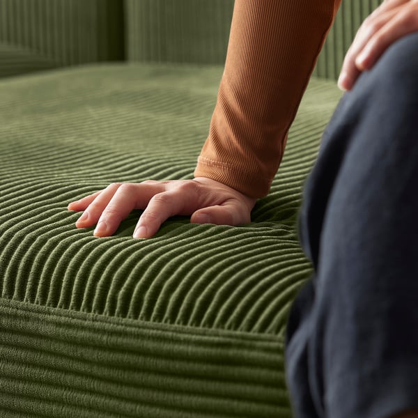 A person touches a green JÄTTEBO sofa. Soft, textured cover in olive. Modern, modular design.