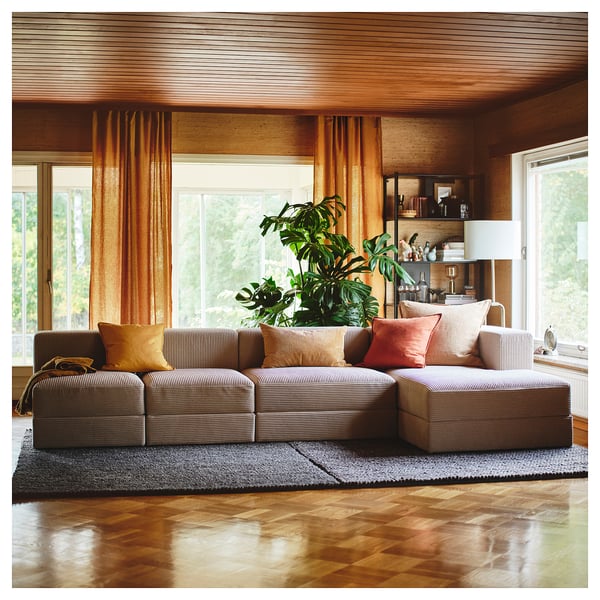 Modern living room with JÄTTEBO modular sofa in grey, orange pillows, wooden floor, large windows, and green plant.