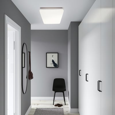 Modern entryway with grey walls and white doors, featuring a JETSTRÖM light panel in the ceiling, a circular mirror, a black chair, and a small rug.