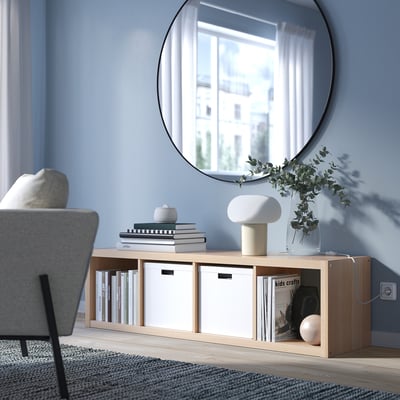 Modern living room with KALLAX storage, mirror, lamp, books, and plants.