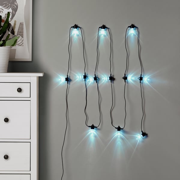KASTTÅG blue lights hang on wall, warm glow near white dresser.