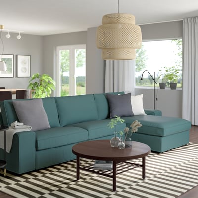 Cosy teal KIVIK sofa, large & comfy, with striped rug, wooden coffee table & hanging lamp. Perfect for relaxation.