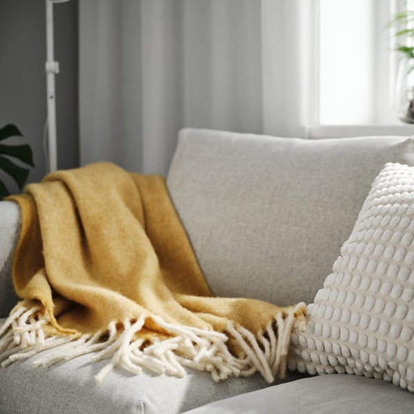 Yellow KLIPPOXEL throw blanket on grey couch, soft, textured, larger than pillows.
