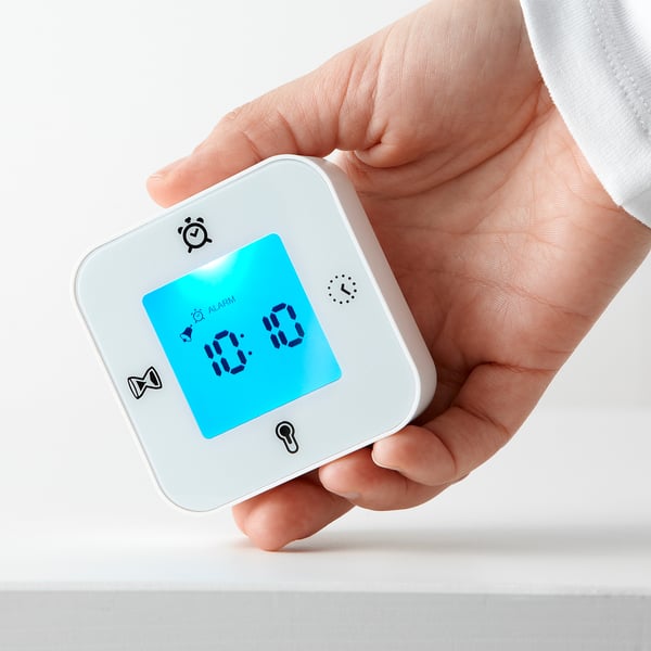 Hand holding a KLOCKIS device, displaying digital alarm clock with time 10:10.