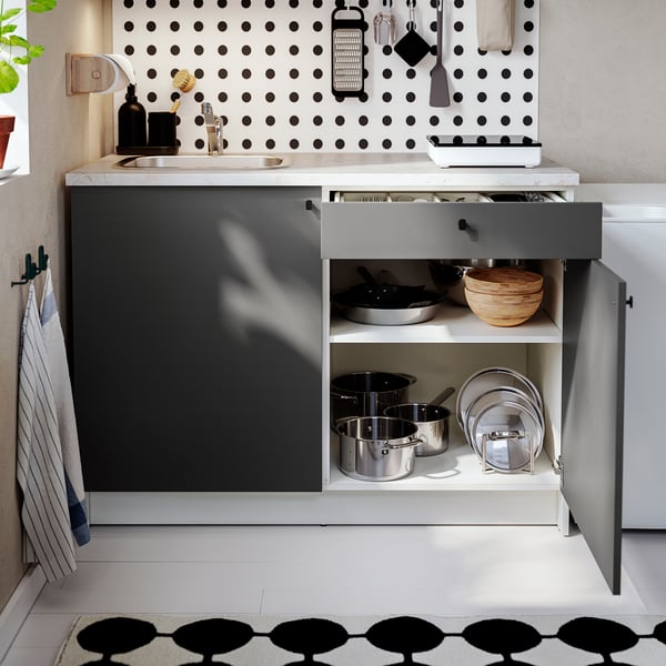 Kitchen setup with open drawer showing pots, pans, and bowls, under polka-dot backsplash.