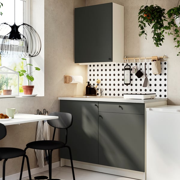 Modern kitchen with black cabinets, polka dot backsplash, hanging plants, and compact design.