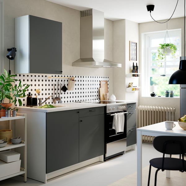 Modern kitchen with dark grey KNOXHULT cabinets, polka dot backsplash, stainless steel appliances, and white dining set near window with plants.