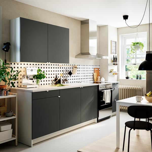Modern kitchen with dark grey cabinets and marble counter. Sink, stove, plants, minimalist decor.