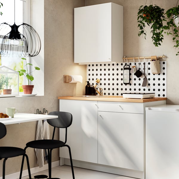 Modern kitchen with white cabinets, black polka dot backsplash, black stools, wooden countertop, hanging plant, and pendant light.