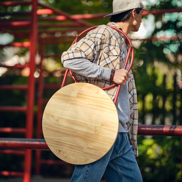 Person carrying folded red KOMPISHÄNG side table, showing portability.