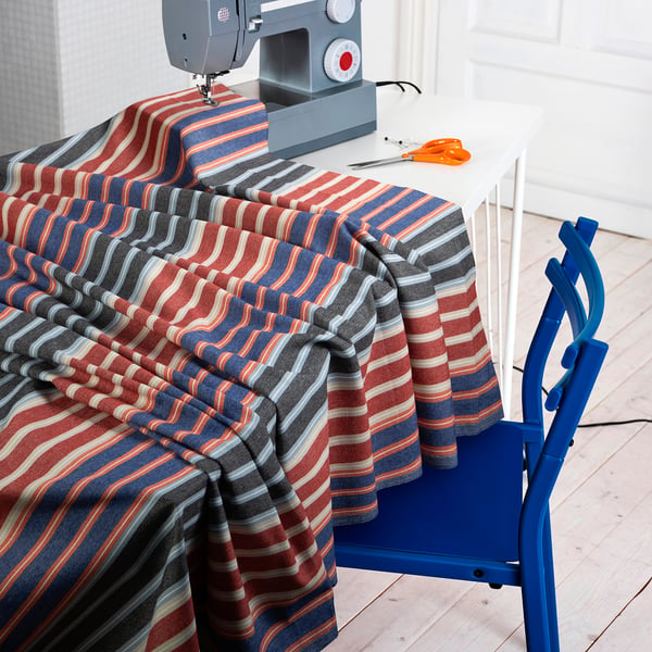 Striped fabric draped on table with sewing machine, scissors, and blue chair, ready for craft or repair project.