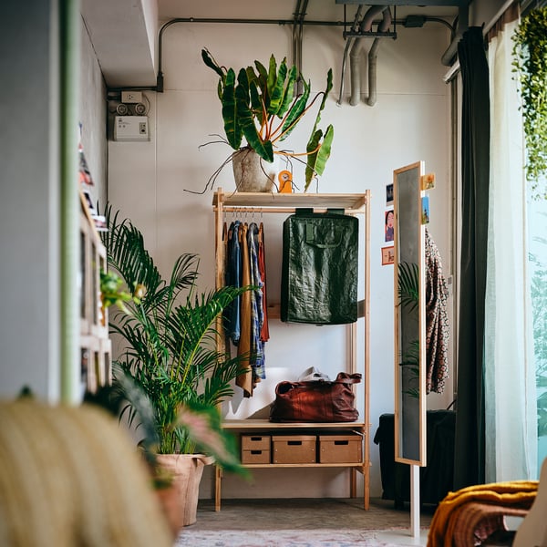 KRONÖREN clothes rack in light wood near window, with bags & plants.