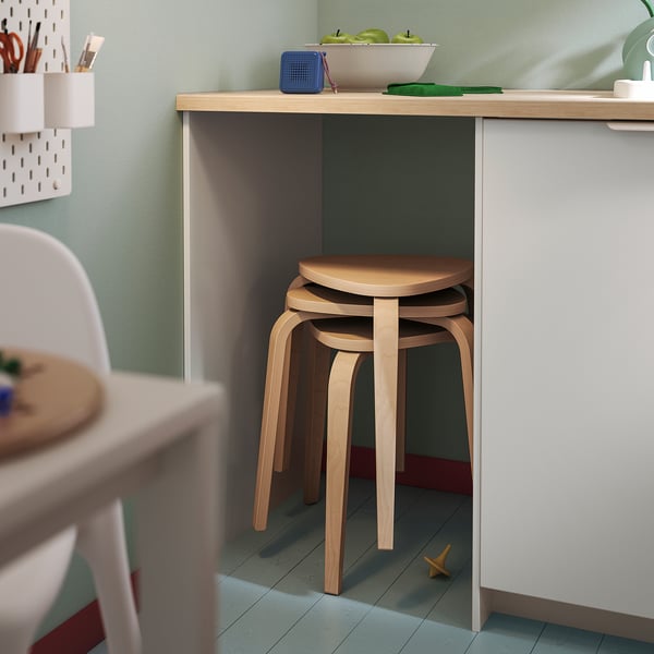 Small wooden KYRRE stool in light finish, stacked under a white desk, showcasing its compact and simple 3-legged design.
