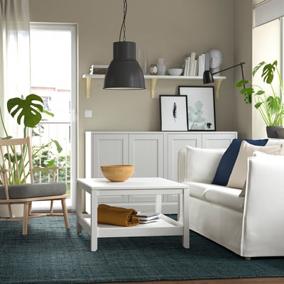Modern living room with LANDBANA jute rug in dark blue. White coffee table, cosy couch, and plants. Black pendant lamp and natural decor.