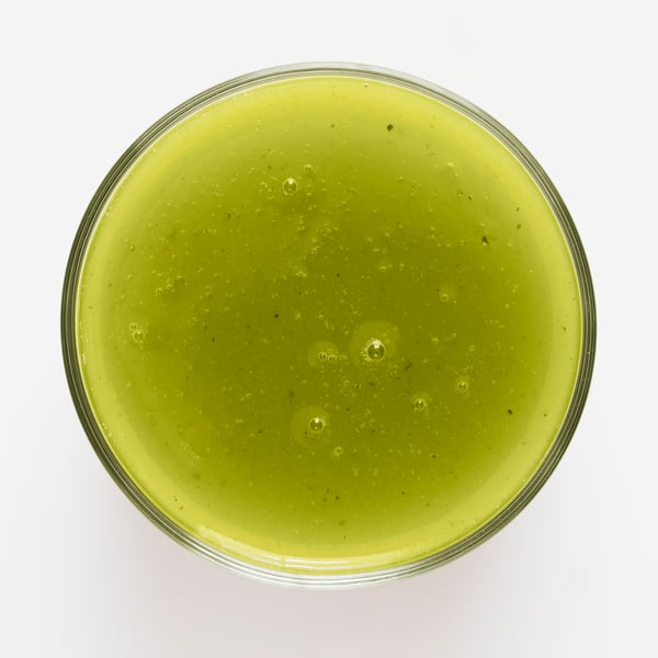 A glass filled with a thick, green LÅNGLUR smoothie, prominently featuring apple and fennel flavours with a hint of turmeric.