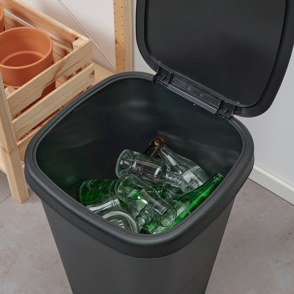 A black recycling bin, LÖVKVAST, holds green bottles; designed with small openings for dual bag use, stands in a room against a wall.