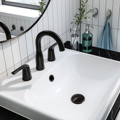 Modern bathroom sink with matte black MACKSJÖN tap, white basin, green soap dispenser, and small plant.