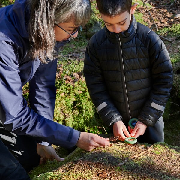 Two people examine nature with a magnifying glass and compass, learning outdoors.