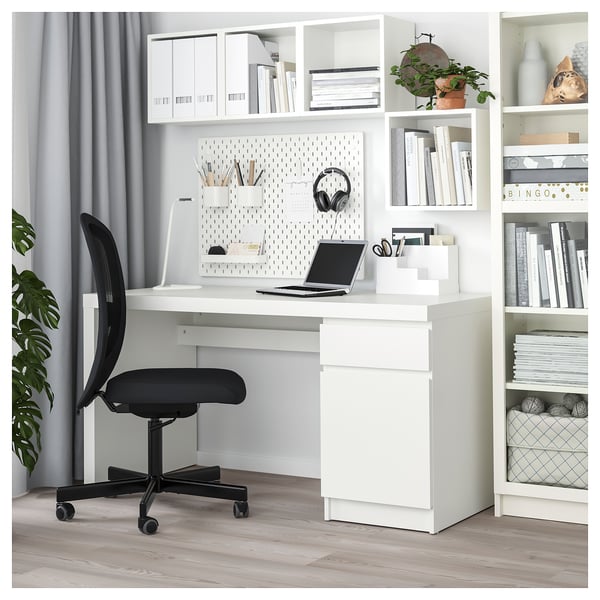 Modern home office with white MALM desk, black swivel chair, storage shelves, and pegboard.