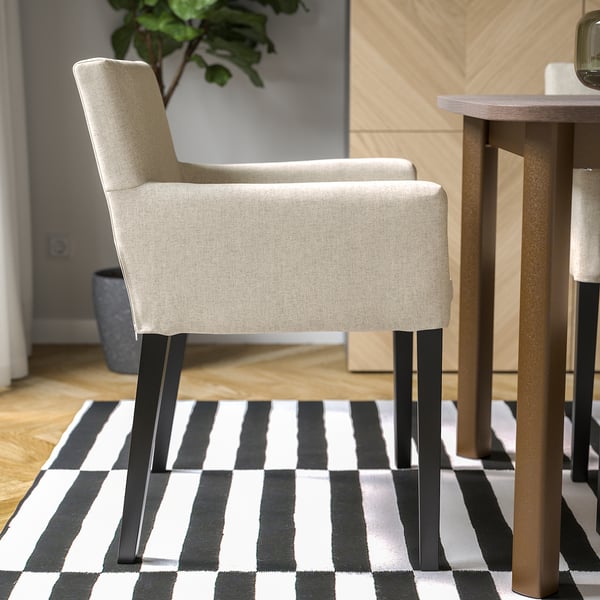 A dining chair with beige fabric and black metal legs on a black and white striped rug.